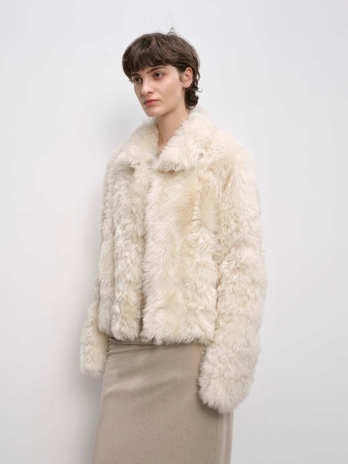 Woman wearing a cream-colored fur jacket against a plain background
