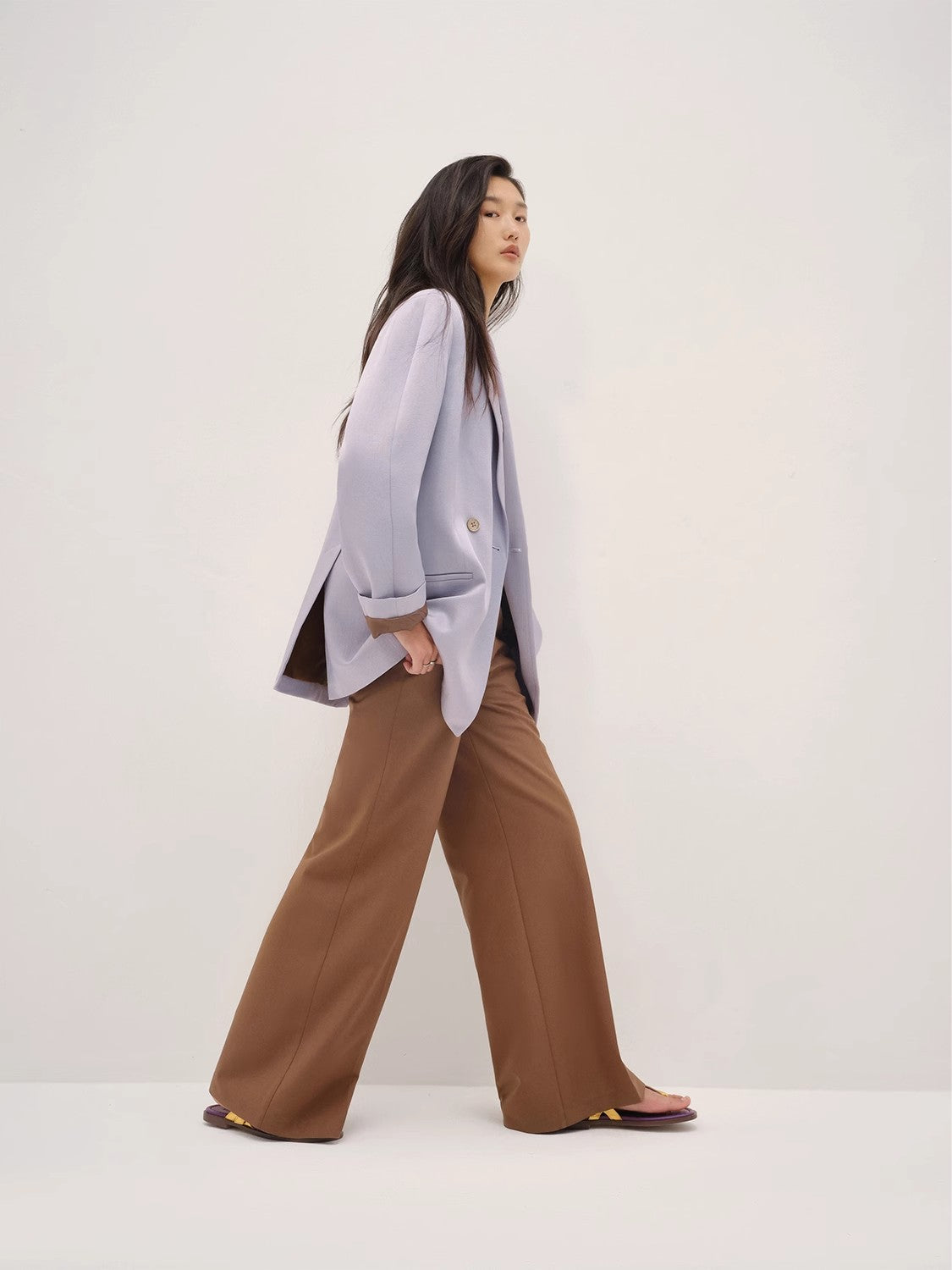 Woman wearing a light gray blazer and brown pants on a white background