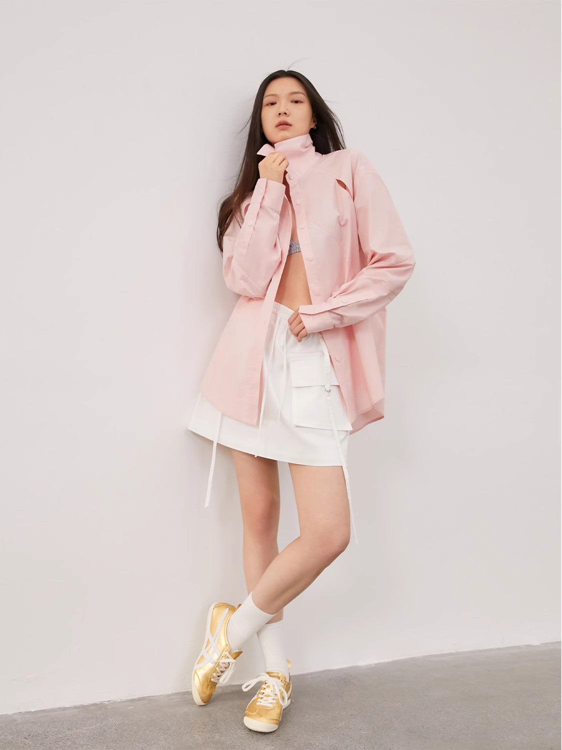 Woman wearing a pink jacket, white shorts, and yellow sneakers against a plain background