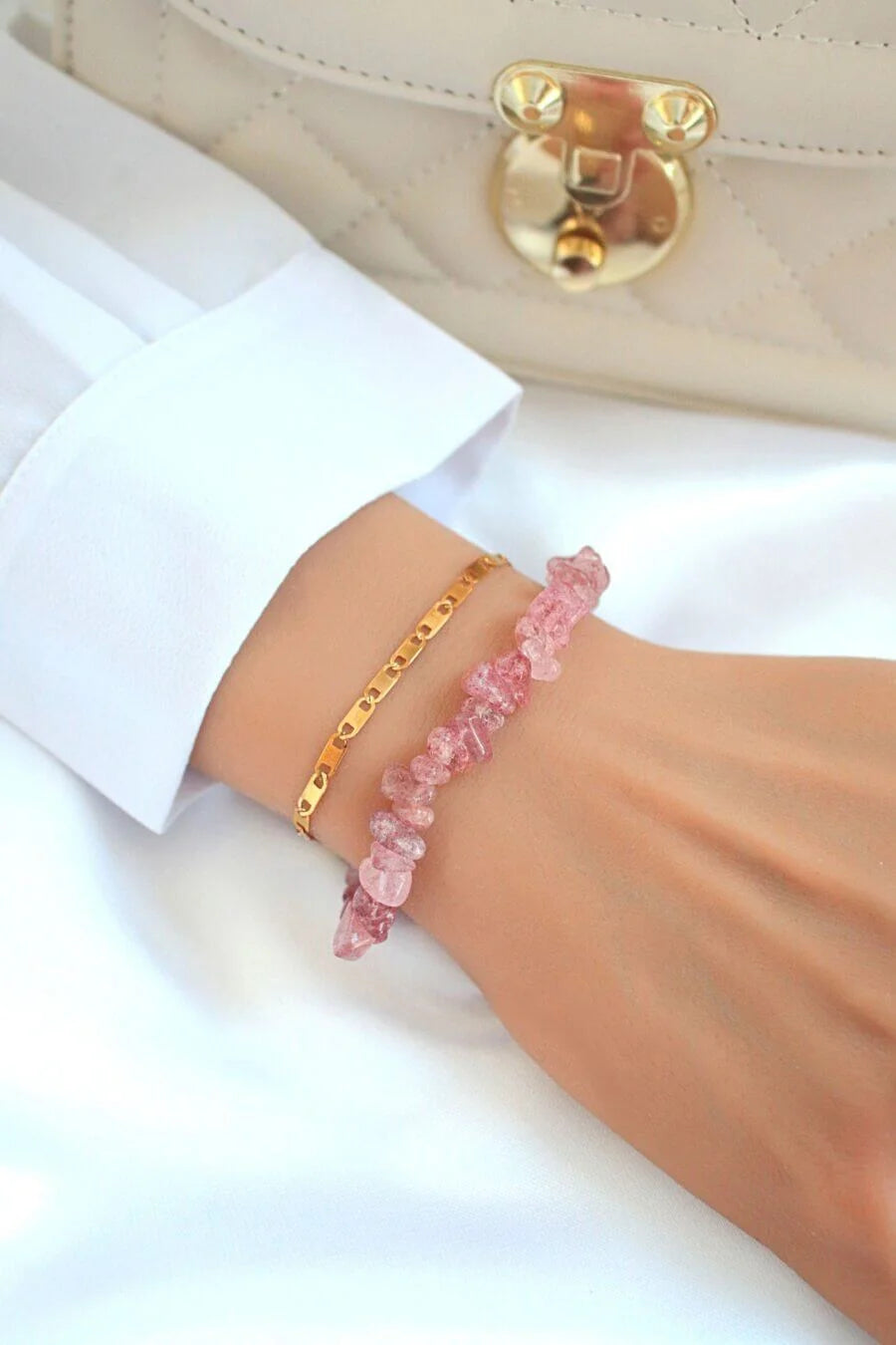 Pink beaded bracelet on a wrist with a gold clasp against a white background