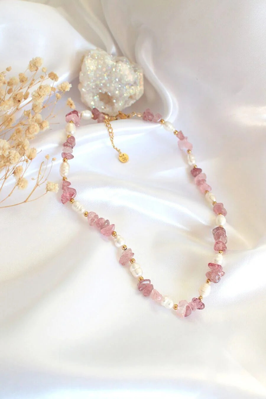 Necklace with pink beads and a white stone pendant on a white fabric background