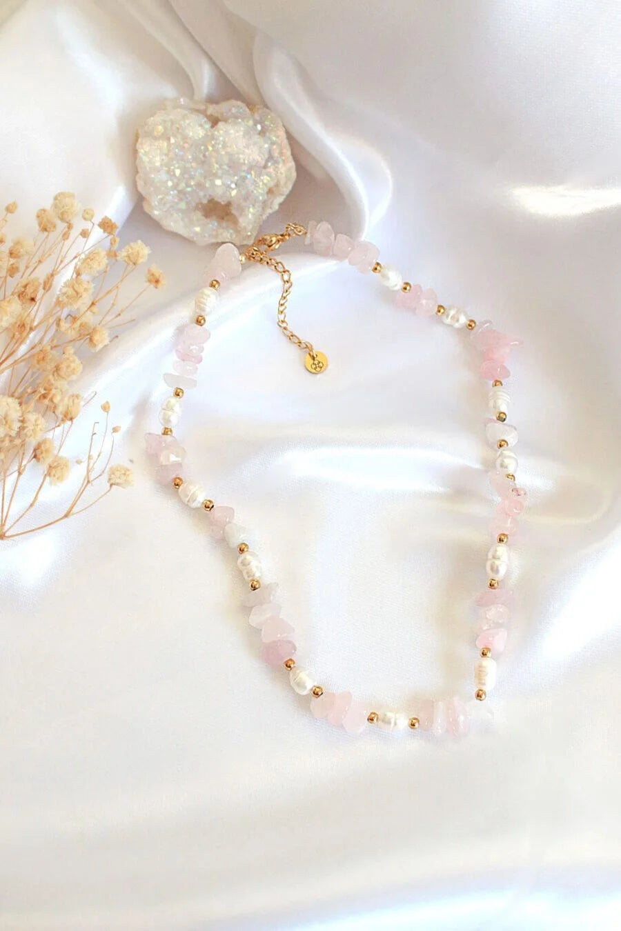 Necklace with pink beads and gold accents on a white fabric background