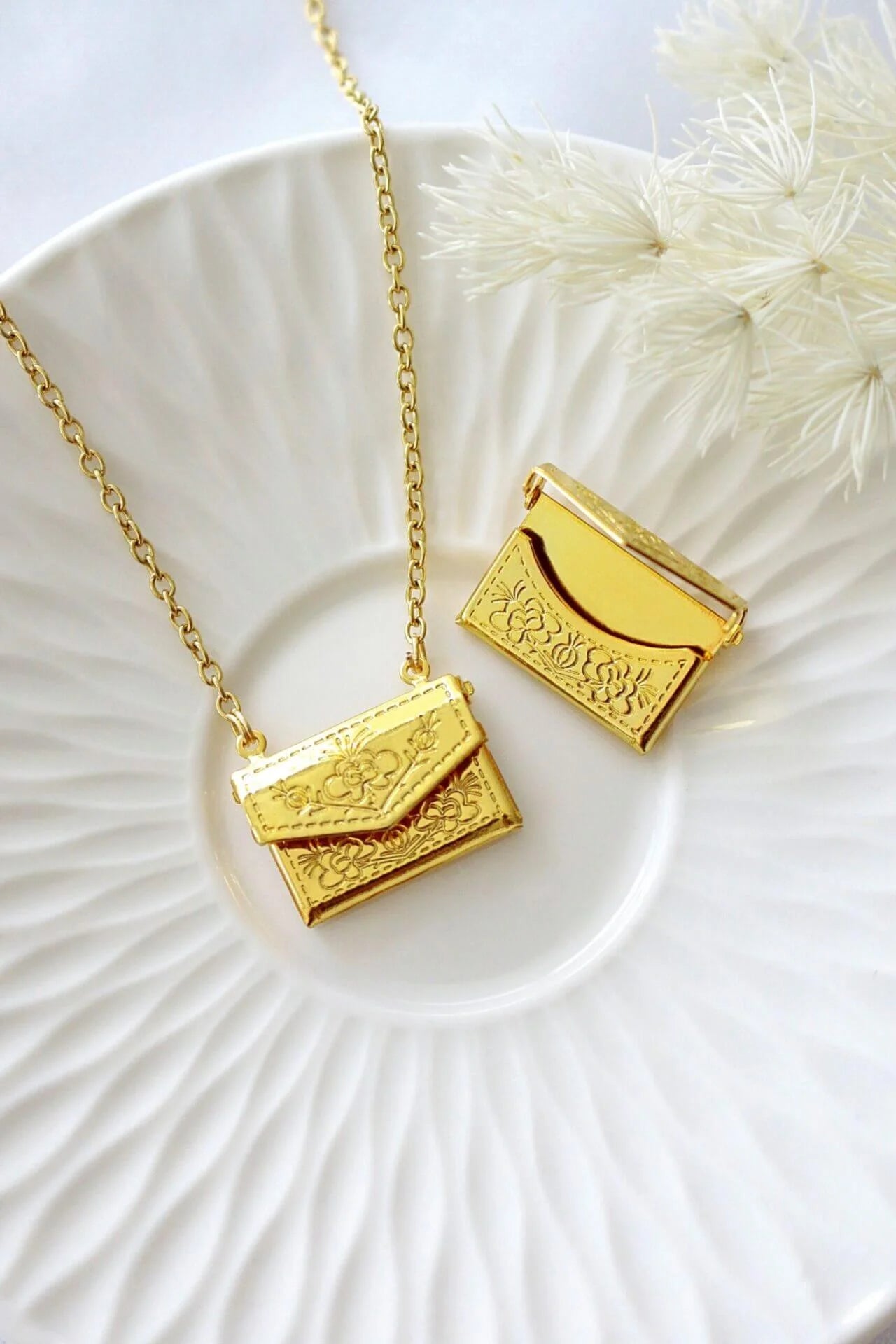Gold necklace with a pendant shaped like a small handbag on a white plate.
