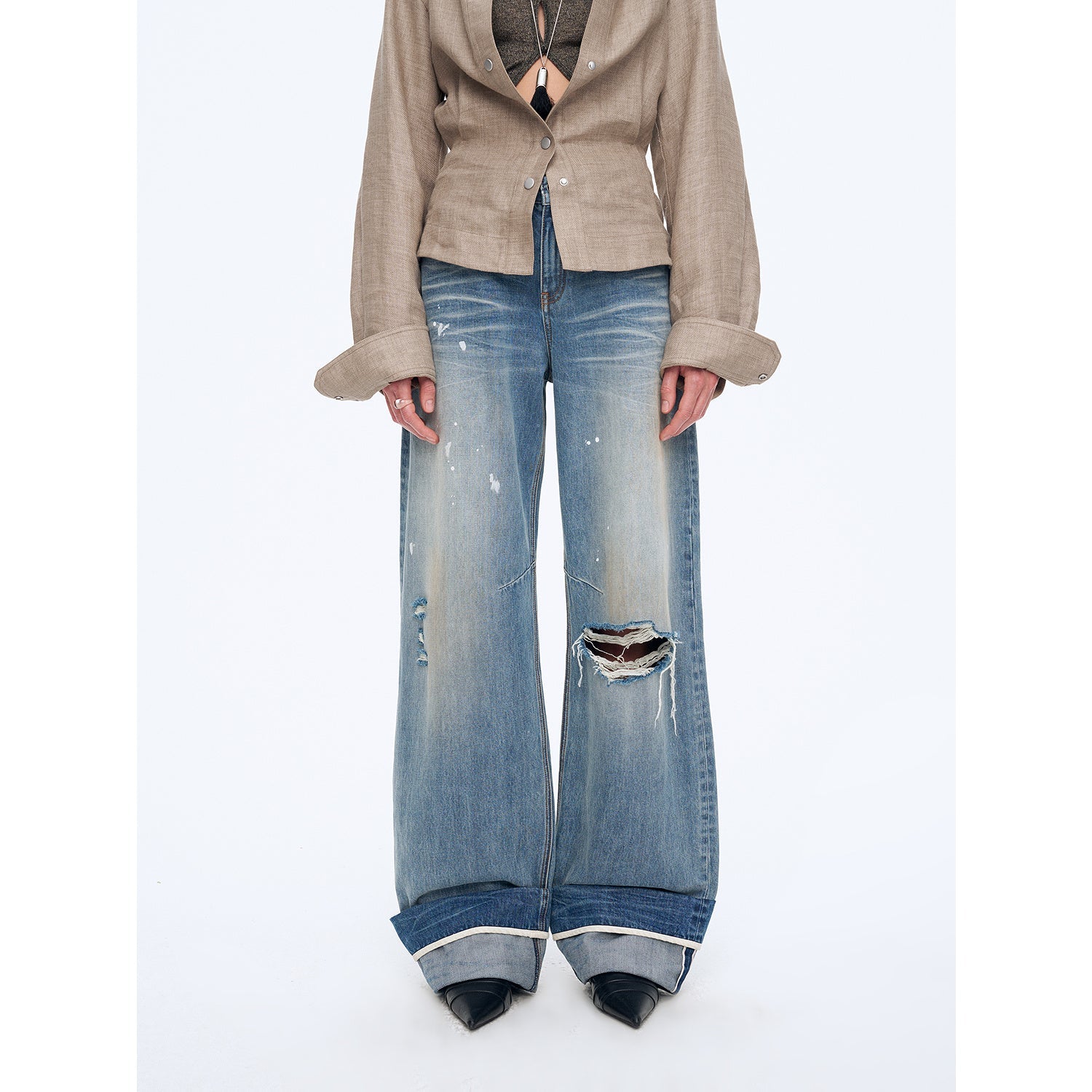 Person wearing a beige blazer and distressed blue jeans on a white background