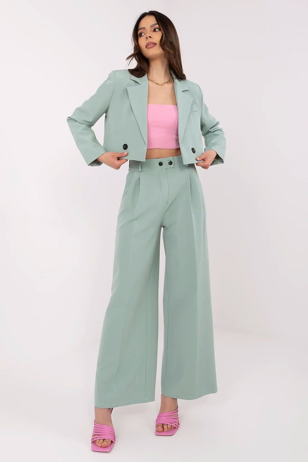 Woman wearing a light green suit with pink top and shoes on a white background