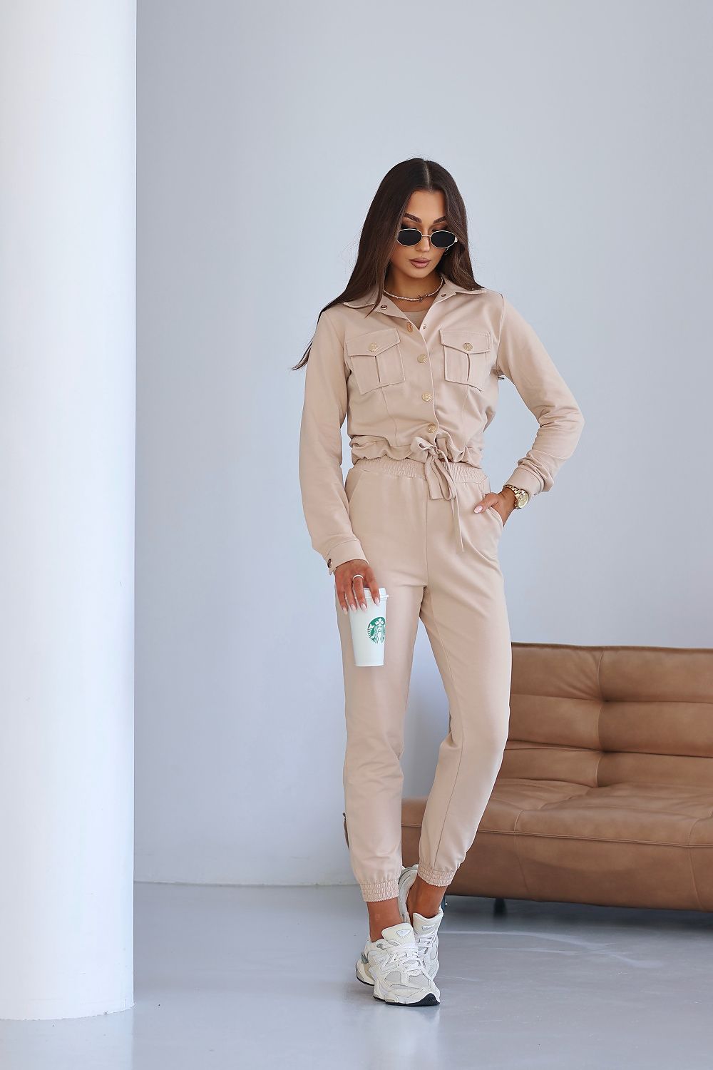 Woman in beige jumpsuit holding a Starbucks cup against a plain background