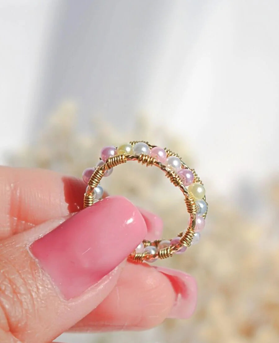 Gold ring with pearls held by a hand against a blurred natural background, featuring 'Divine Dulcet Fine Jewelry'.