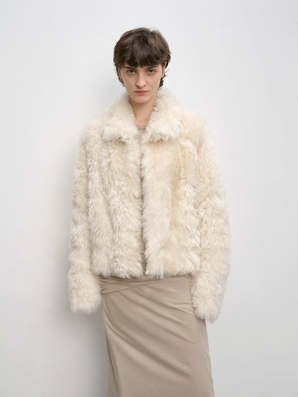 Person wearing a cream fur jacket against a plain background