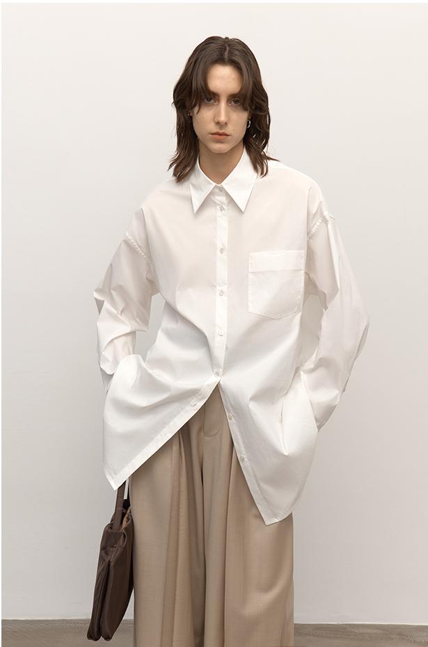 Person wearing an oversized white shirt and beige pants against a plain background