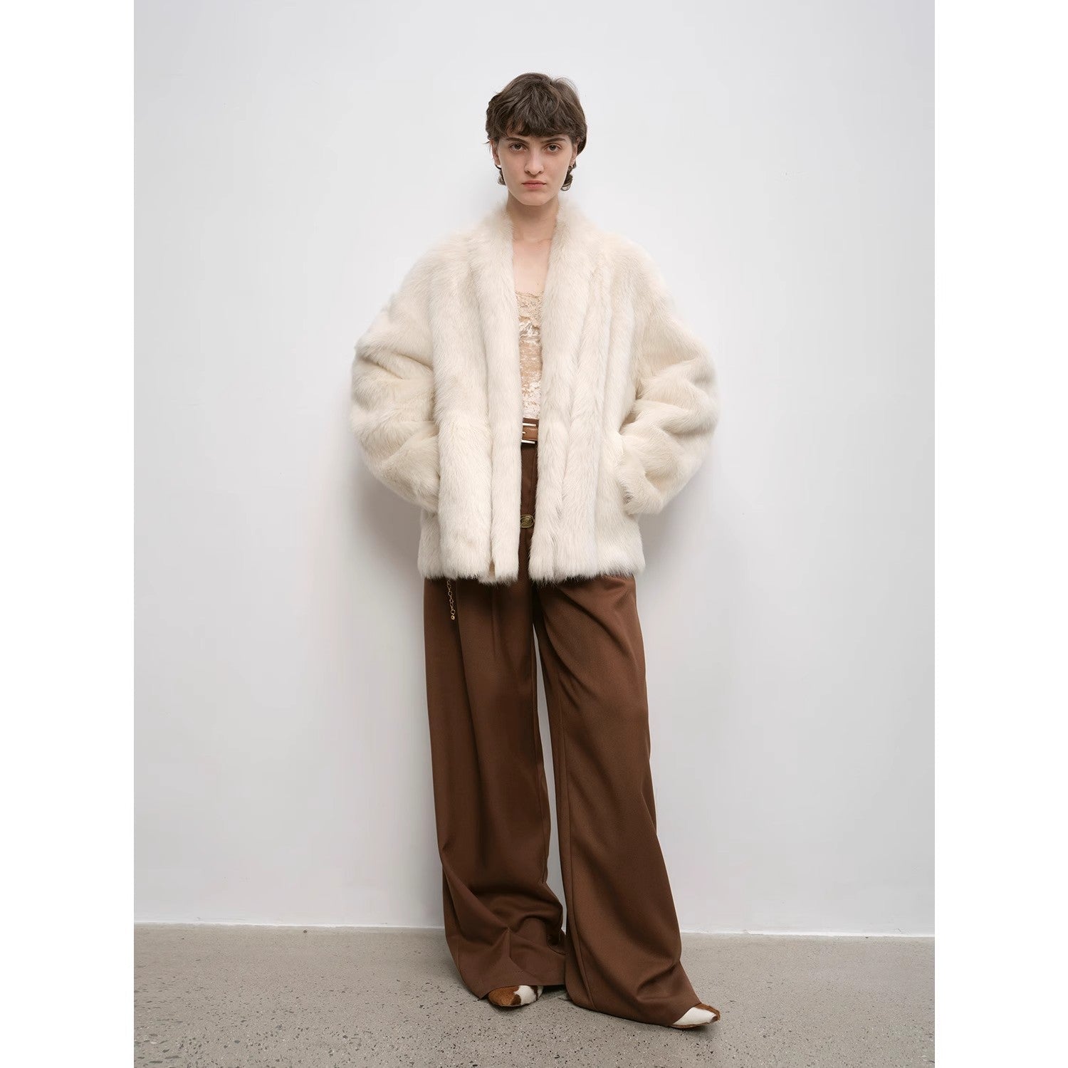 Person wearing a white fluffy coat and brown pants against a plain background