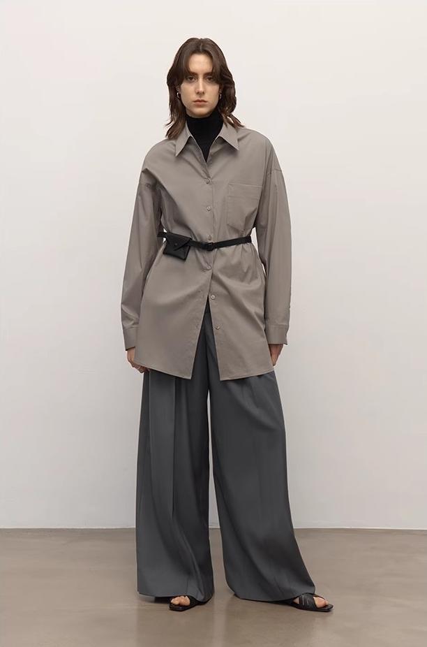 Model wearing a beige trench coat and gray pants against a white background