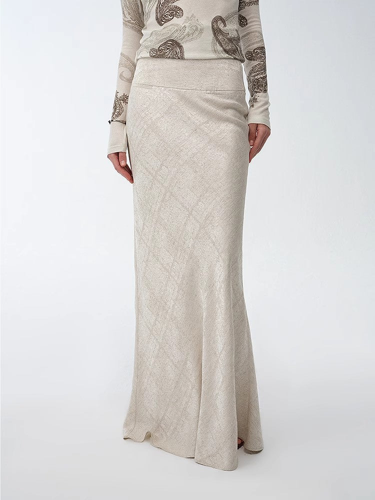 Person wearing a long beige skirt with a patterned top on a white background