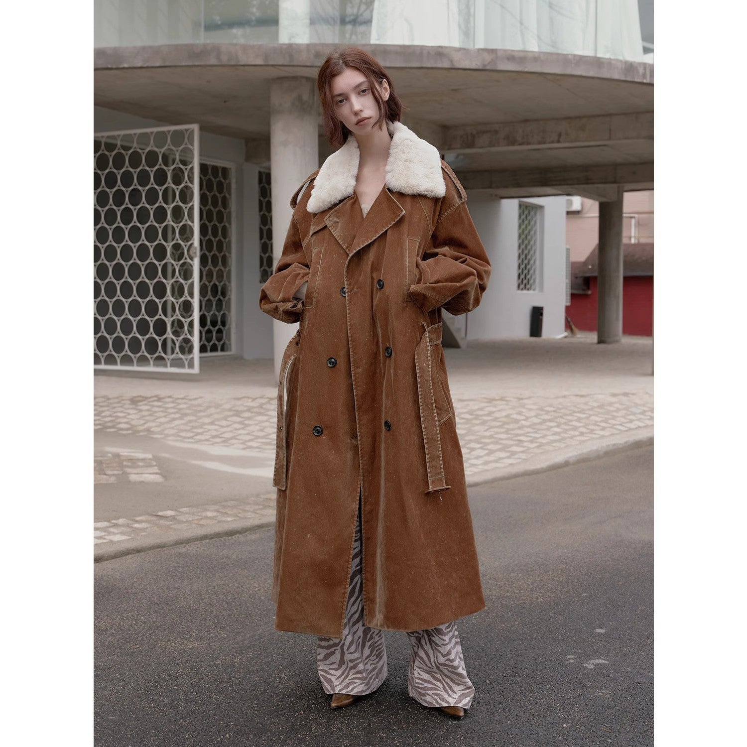Person wearing a brown coat with white fur collar in an urban setting