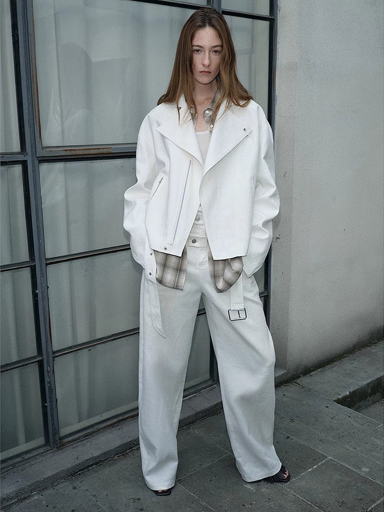 Person wearing a white outfit with plaid gloves standing against a neutral wall.