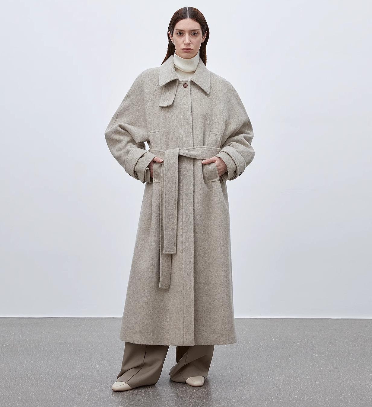 Woman wearing a long beige coat with a belt against a white background