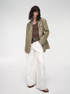 Person wearing a green jacket, brown top, and white pants on a white background
