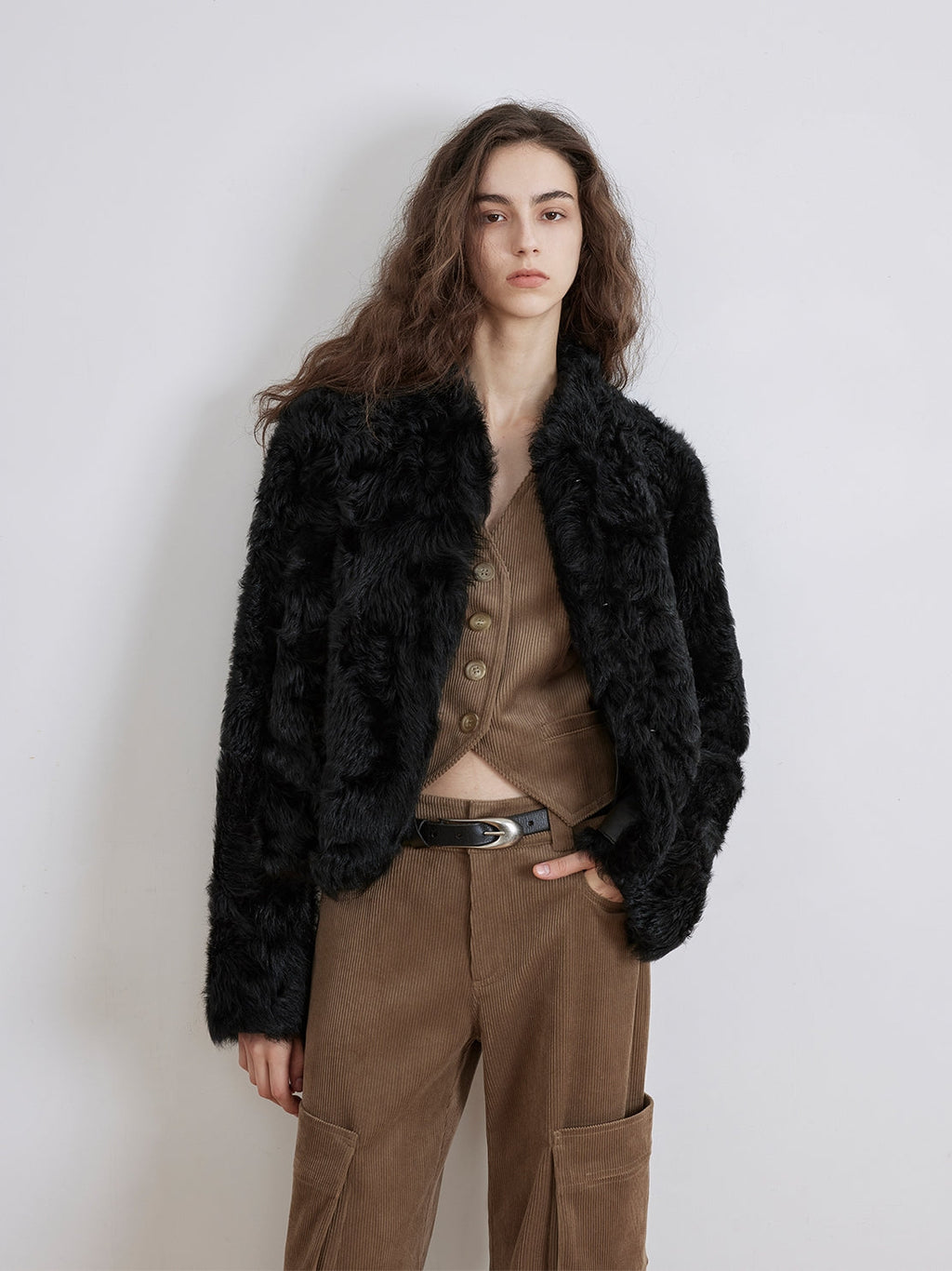 Woman wearing a black fur jacket and brown pants against a white background
