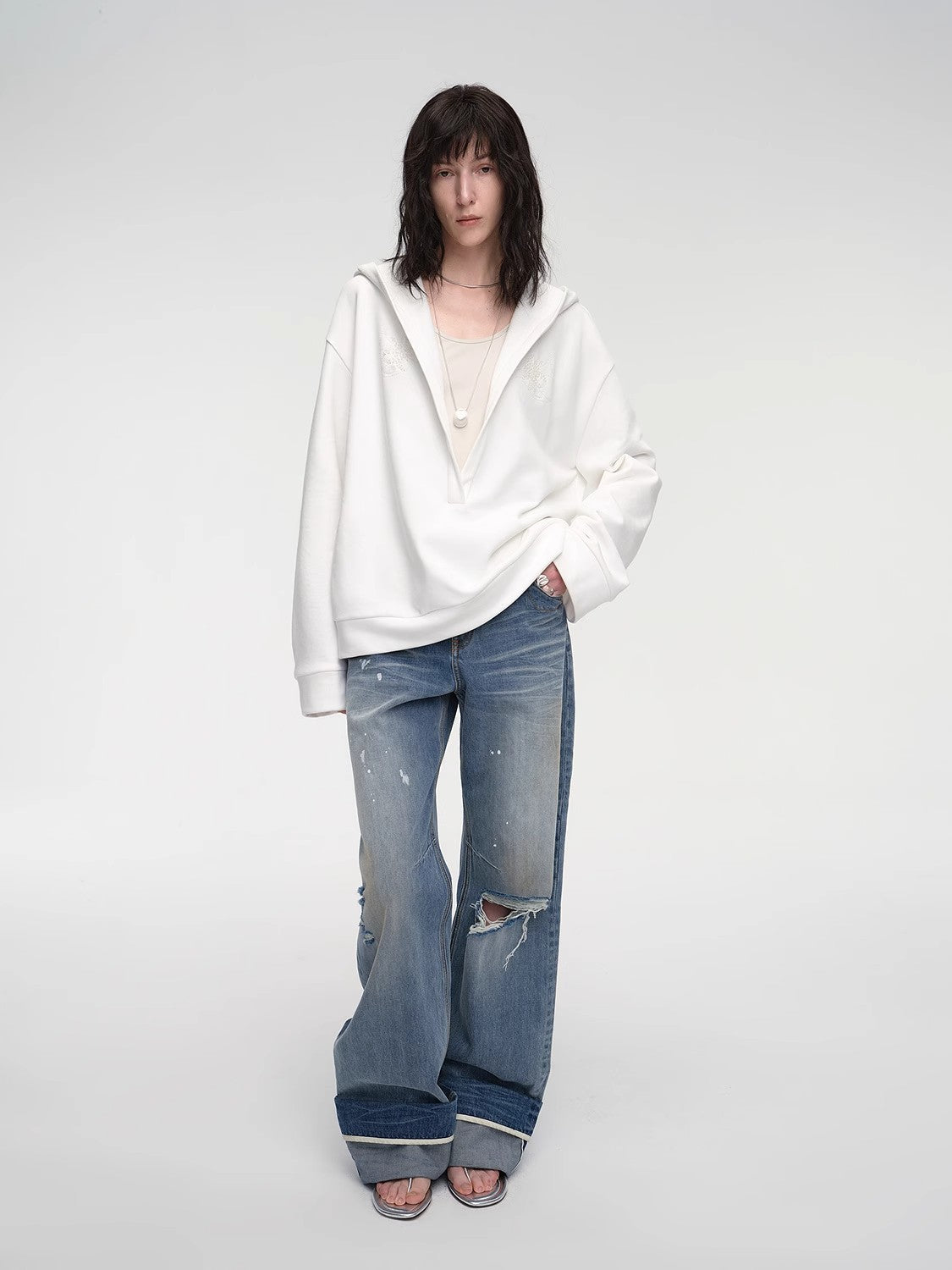 Person wearing a white hoodie and blue jeans on a plain background