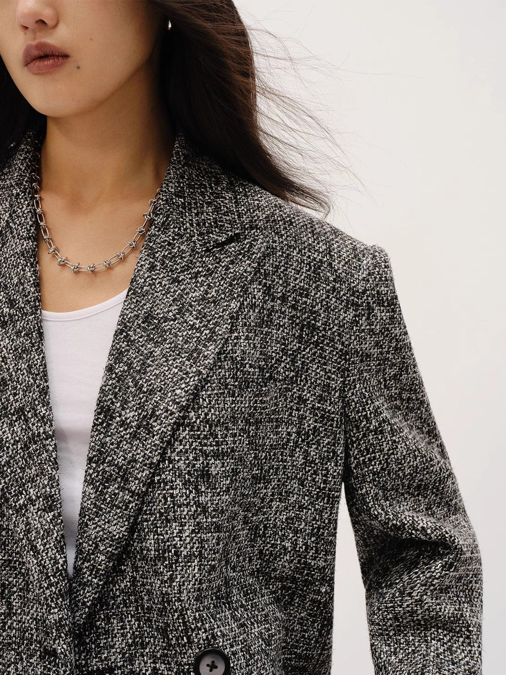 Person wearing a textured blazer over a white top on a plain background