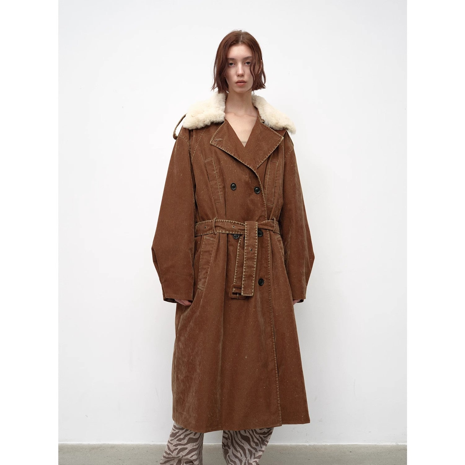 Person wearing a brown coat with white fur trim on a white background