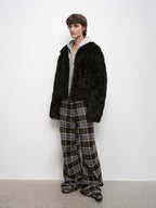 Person wearing a black fluffy coat and plaid pants against a white background