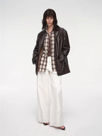 Person wearing a brown jacket, plaid shirt, and white pants on a white background
