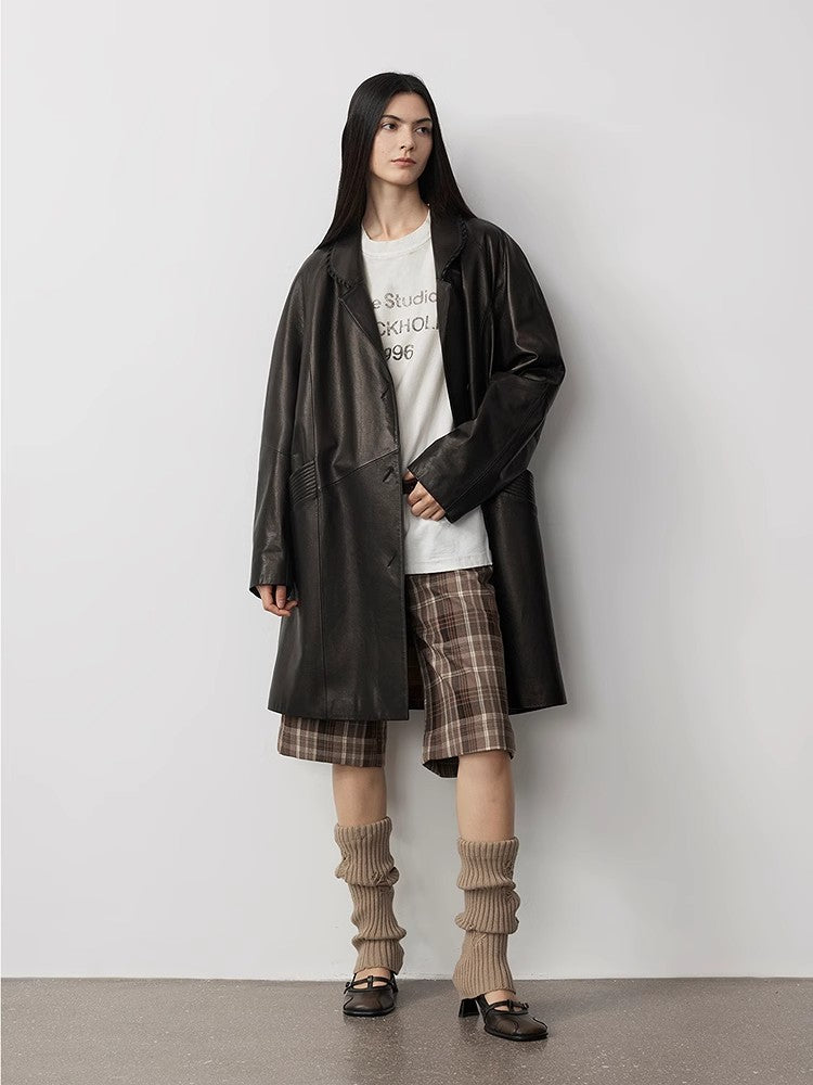 Person wearing a long dark coat, plaid skirt, and knee-high socks against a plain background