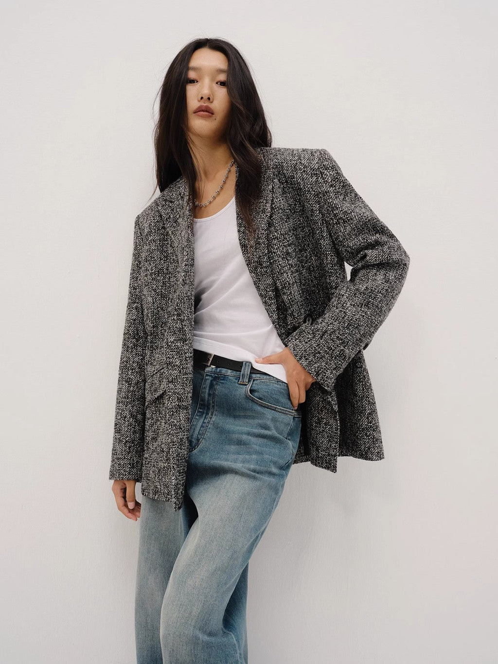 Woman wearing a gray blazer, white shirt, and blue jeans against a plain background