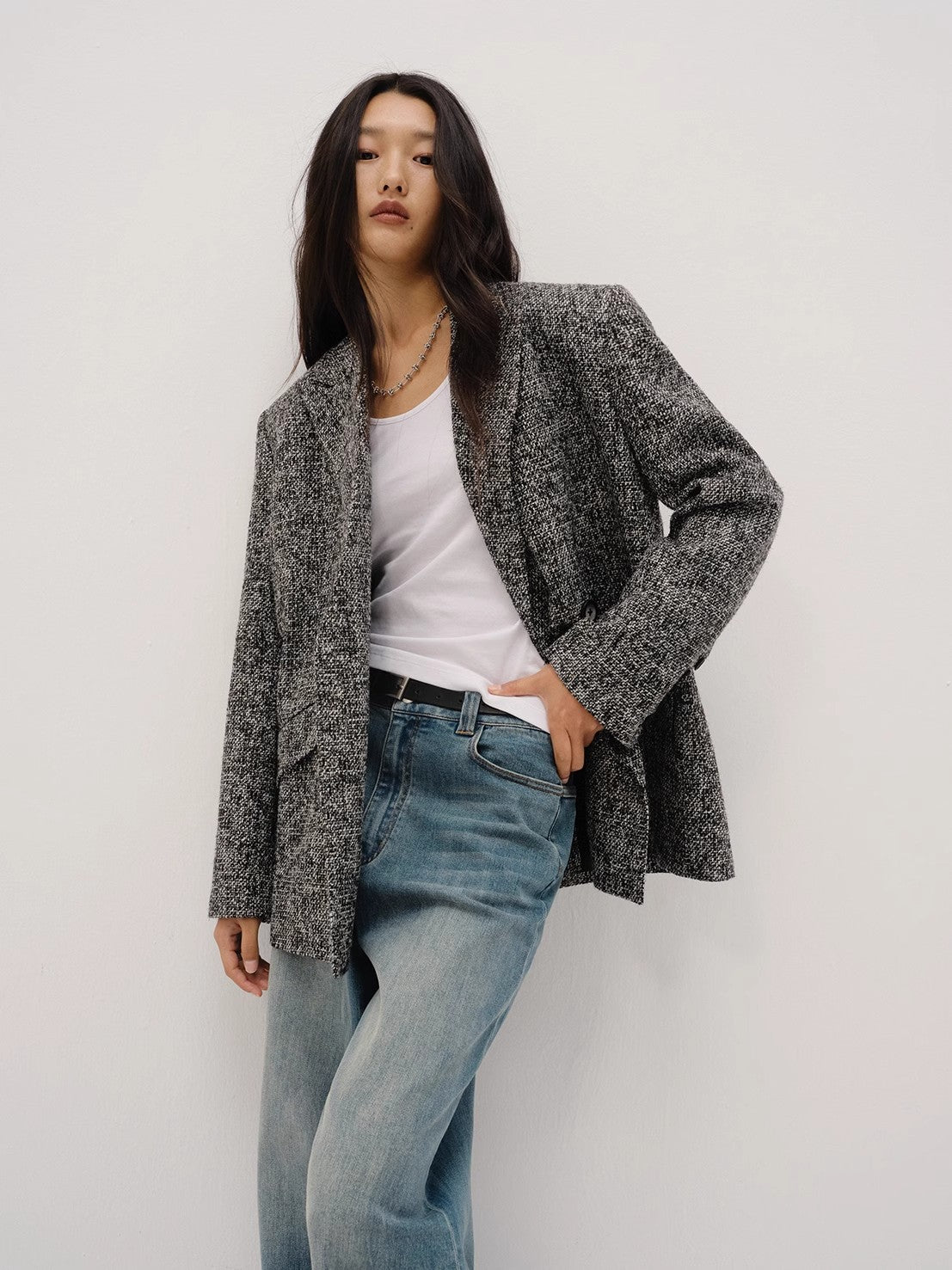 Woman wearing a gray blazer, white shirt, and blue jeans against a plain background