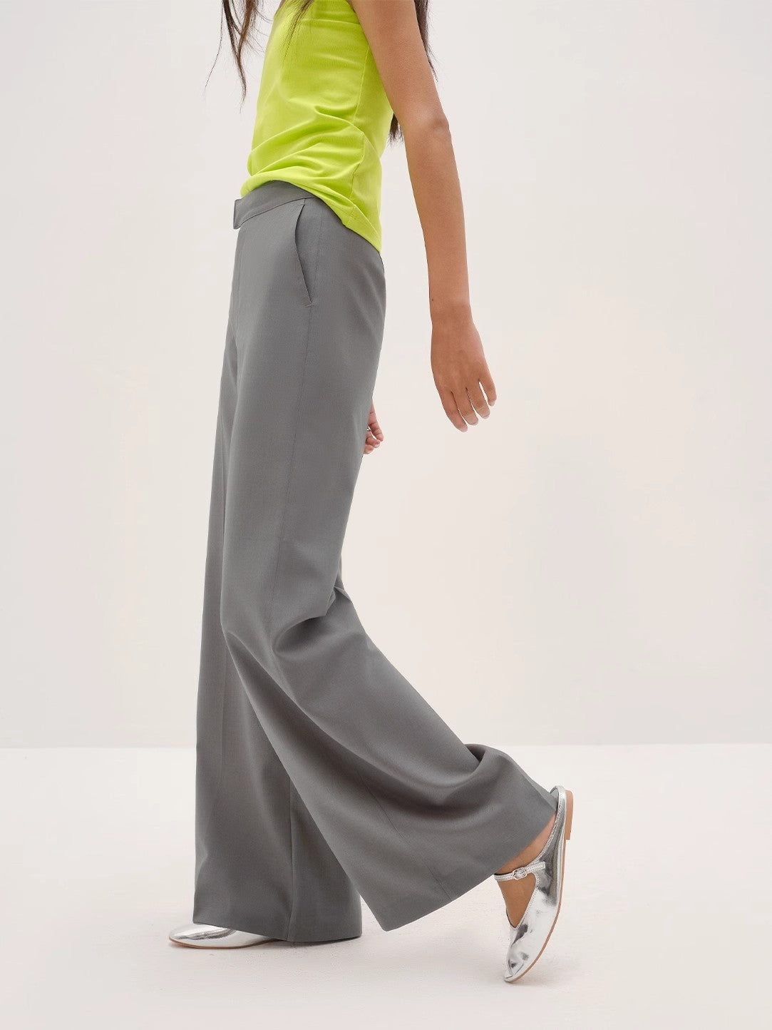 Person wearing gray wide-leg pants and a bright green top on a white background