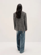 Person wearing a textured blazer and blue jeans on a white background