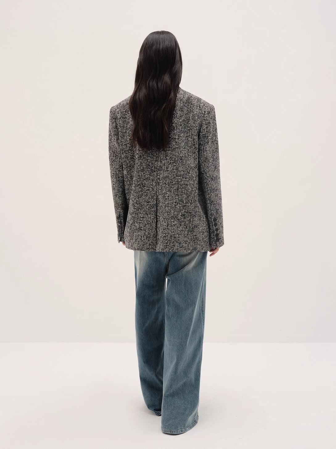 Person wearing a textured blazer and blue jeans on a white background