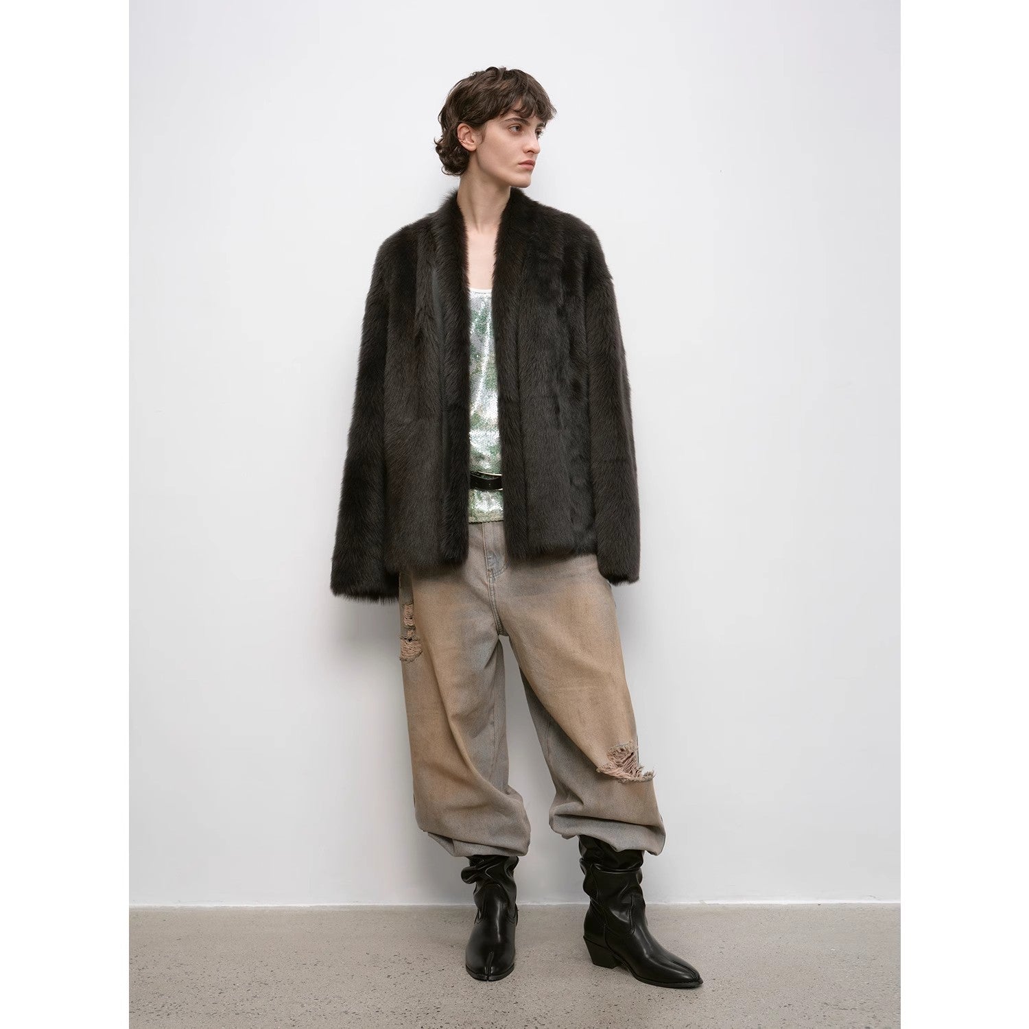 Person wearing a dark fur coat, light pants, and black boots against a white background