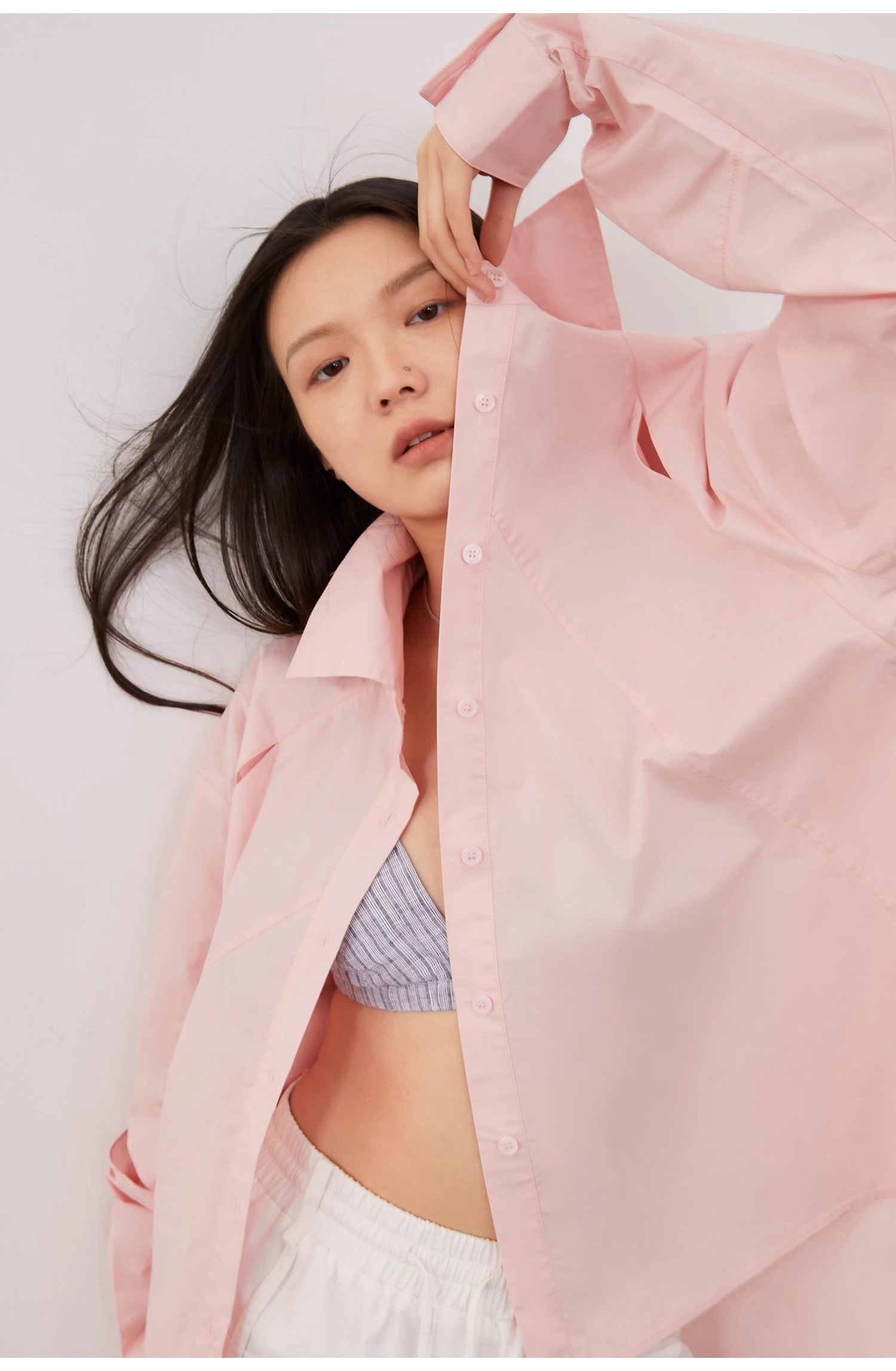 Woman wearing a light pink shirt over a gray top with a white background