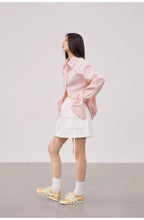 Person wearing a pink jacket and white skirt with yellow shoes on a plain background