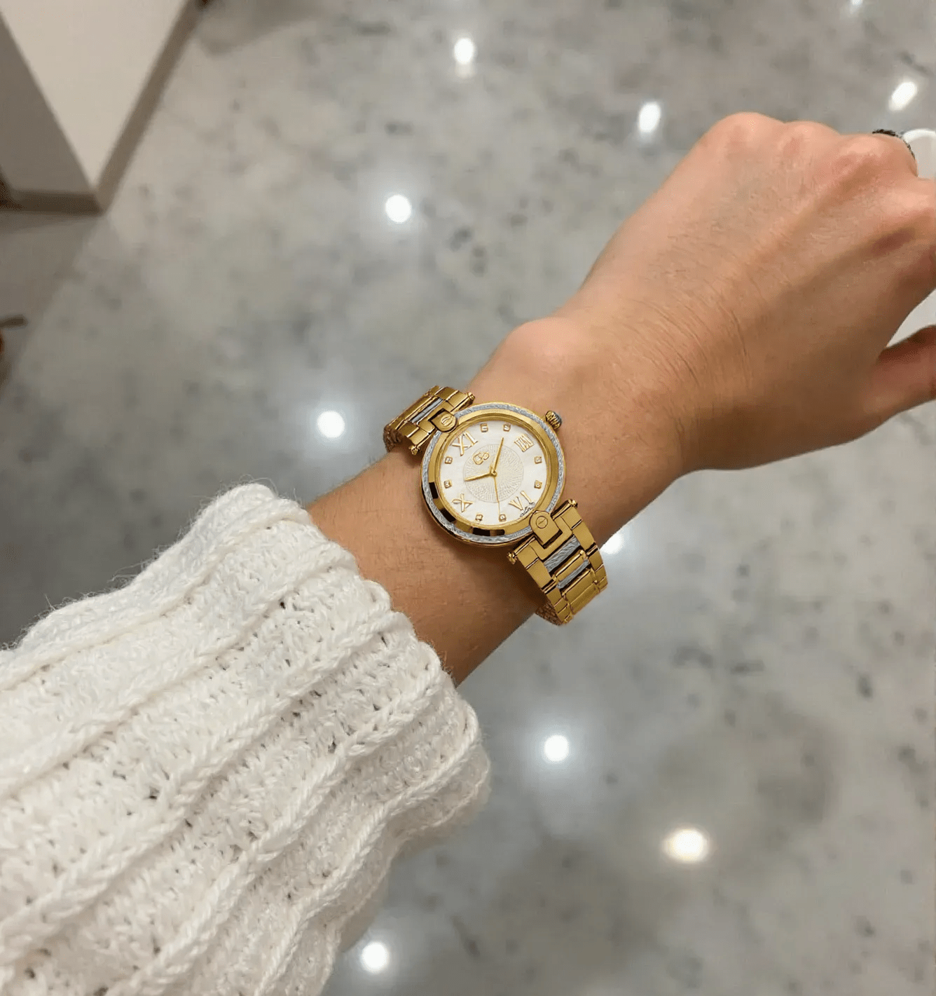 Elegant ladies' gold-tone stainless steel wristwatch with a white mother-of-pearl dial, sapphire glass, and stone-set face, water-resistant up to 100 meters.