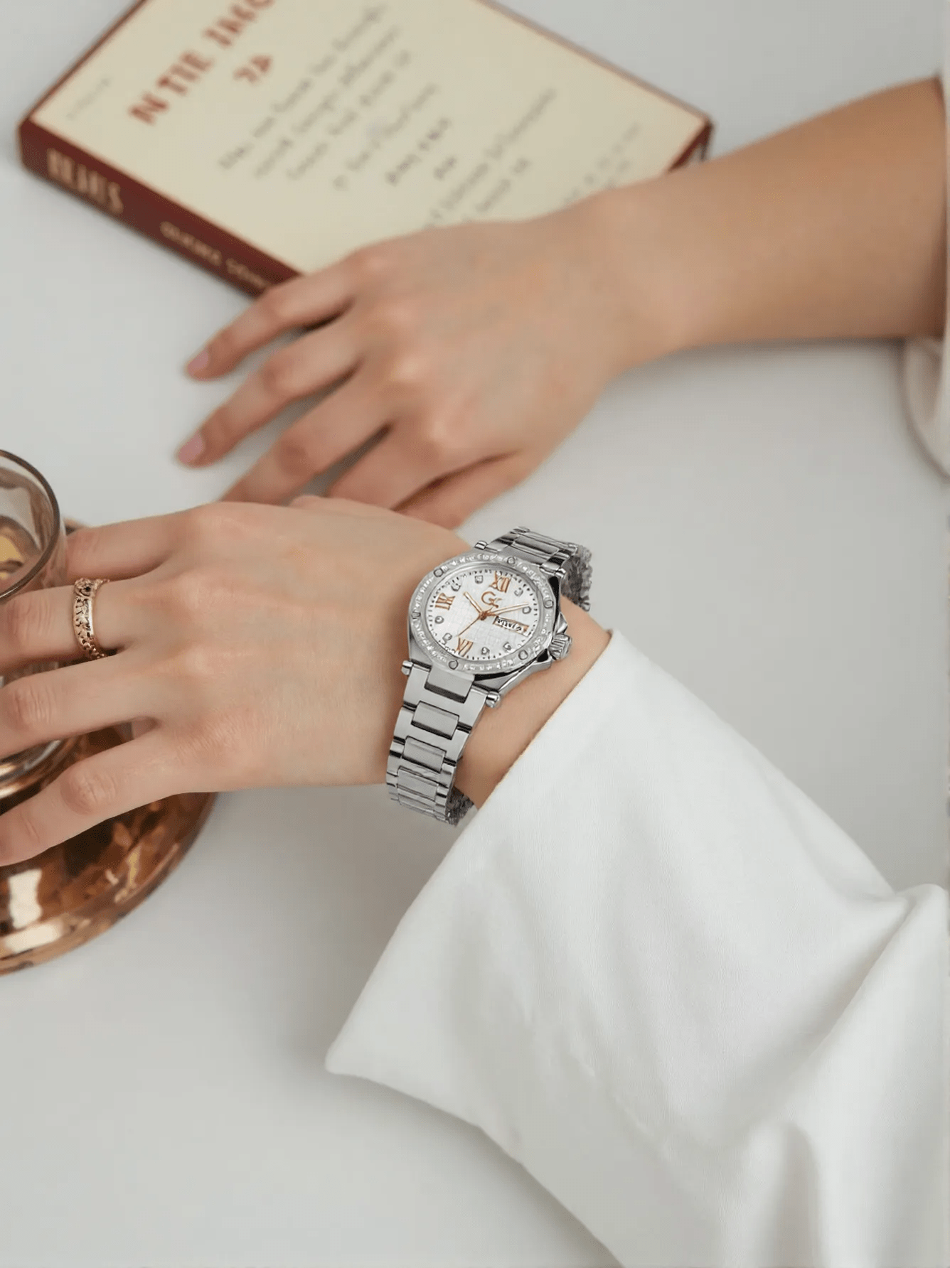 Stylish multifunctional ladies' silver-tone stainless steel watch with white dial, sapphire glass, stone-set case and face, featuring weekday and date display, water-resistant to 100 meters.