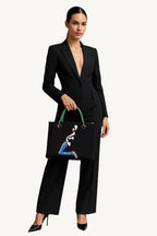 Woman holding a black handbag with a graphic design against a plain background