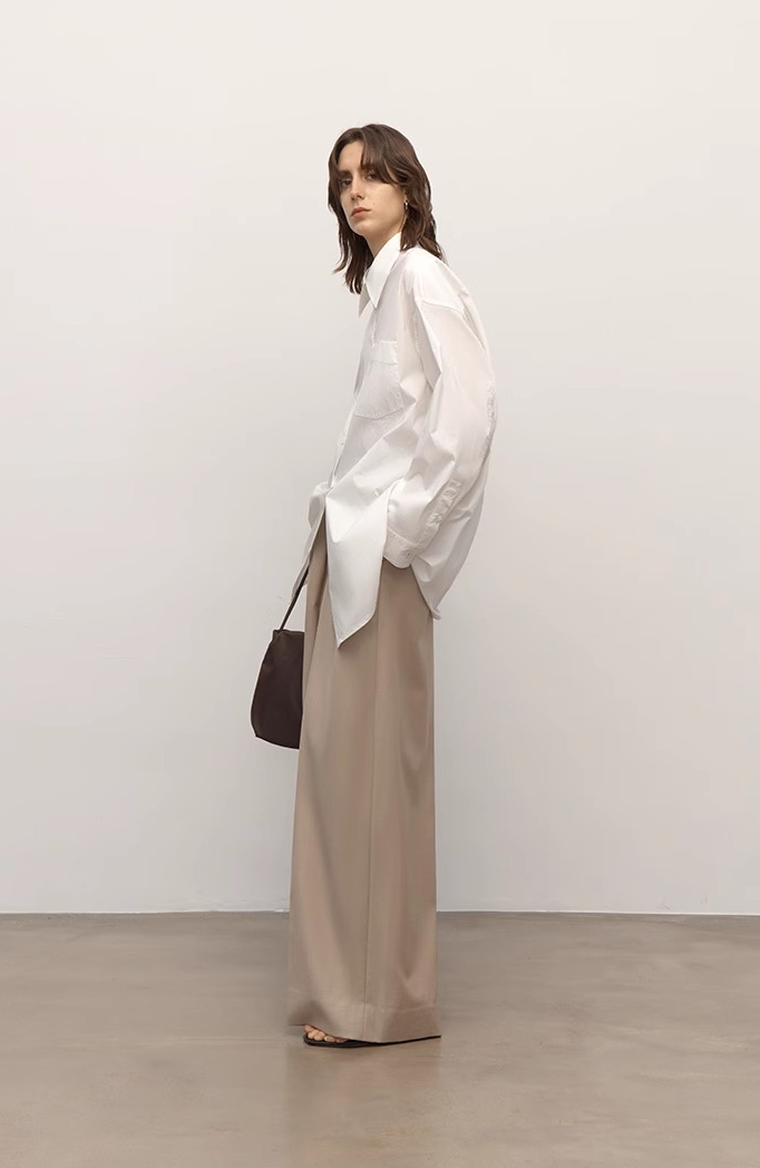 Woman wearing a white blouse and beige pants against a plain background