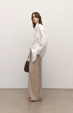 Woman wearing a white blouse and beige pants against a plain background