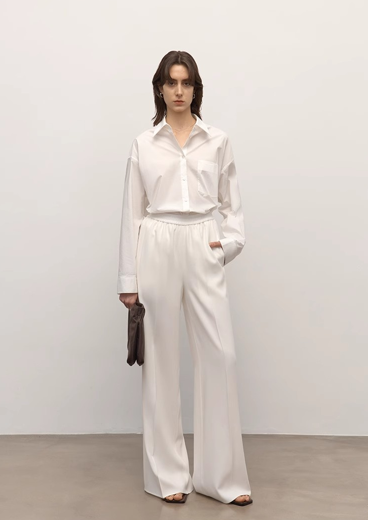 Woman wearing a white shirt and pants against a plain background