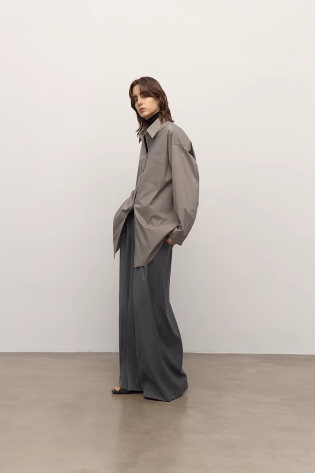 Person wearing a gray coat and wide-leg pants against a plain background
