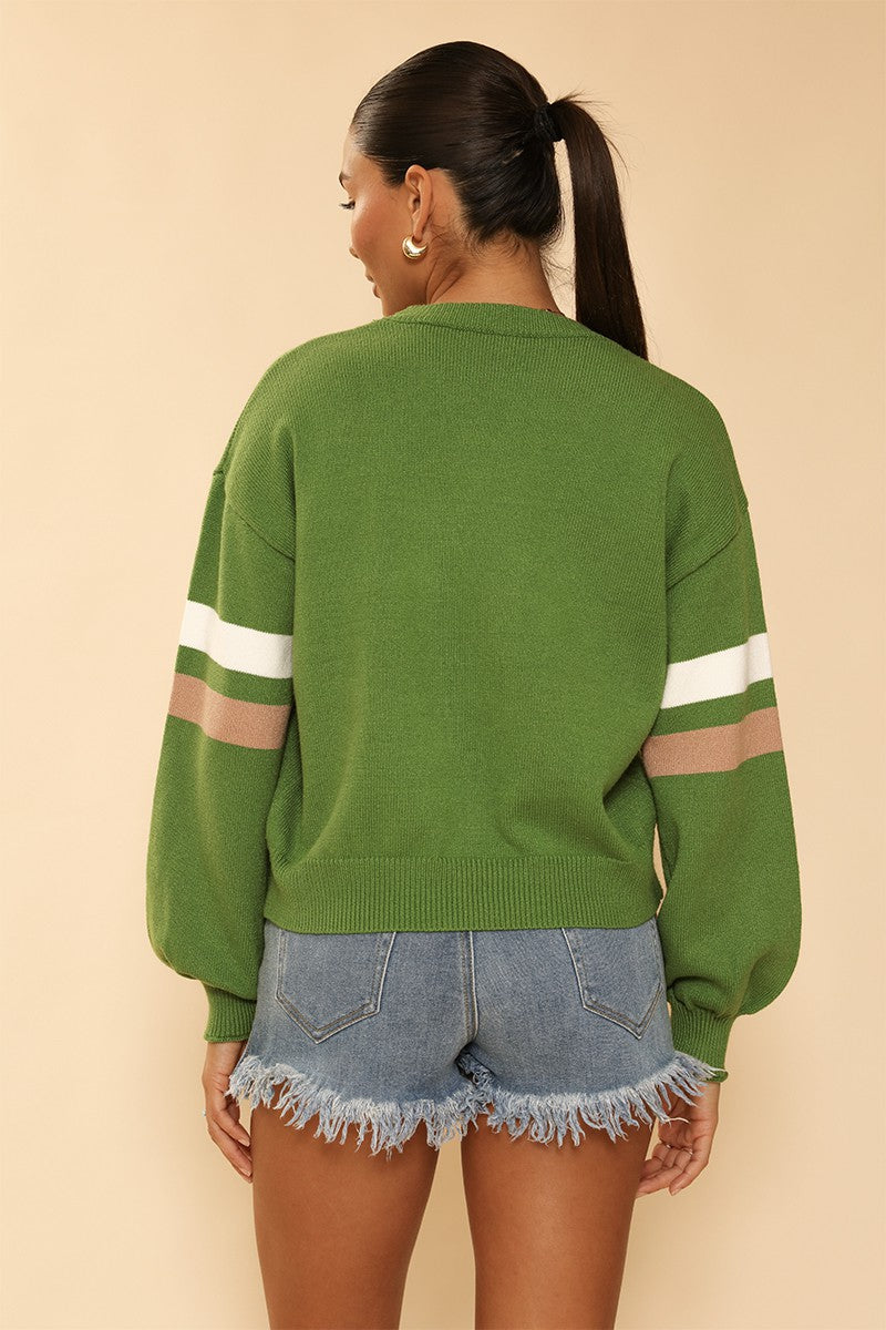Person wearing a green sweater with white and brown stripes on sleeves against a beige background