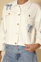 White denim jacket with blue bow designs on a beige background