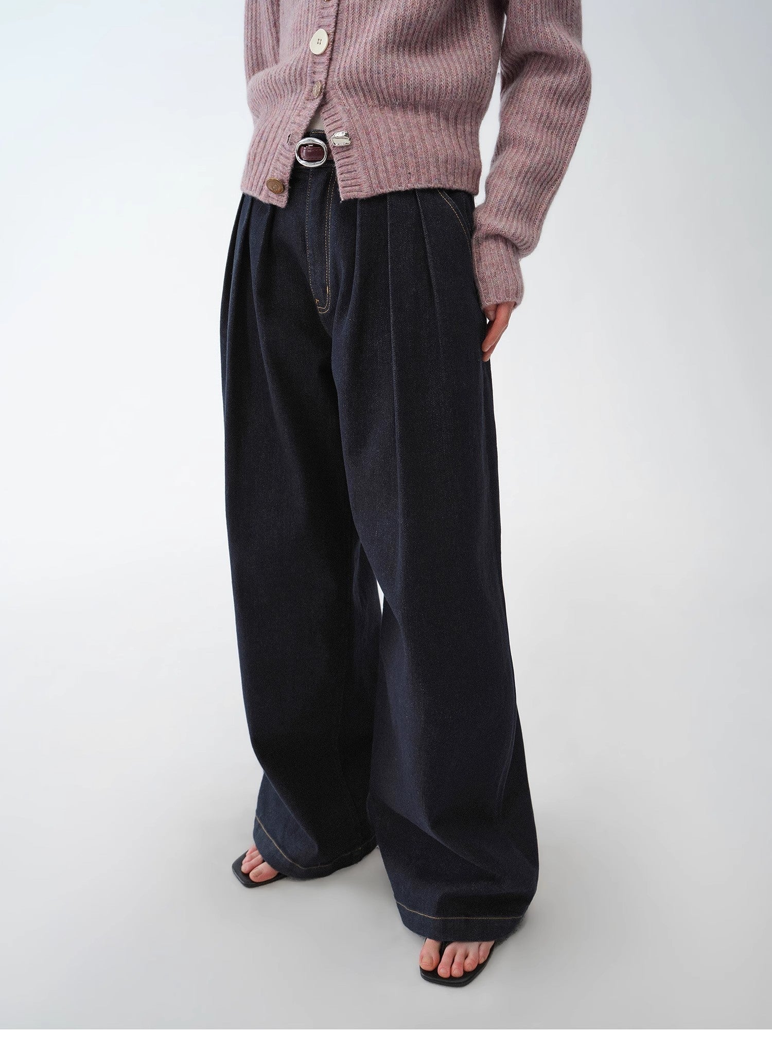 Person wearing a pink cardigan and dark wide-leg pants on a white background