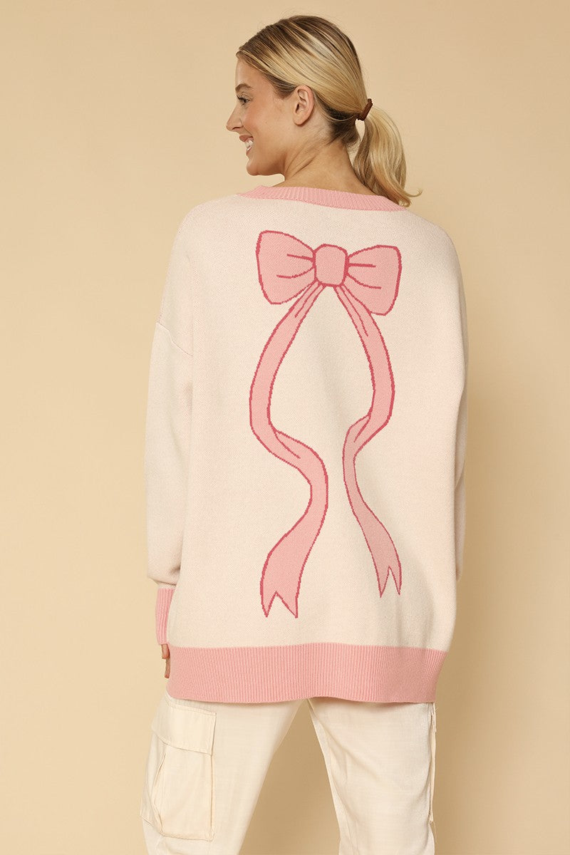 Woman wearing a cream sweater with a pink bow design on a beige background
