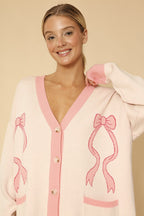 Woman wearing a pink cardigan with bow designs on a beige background