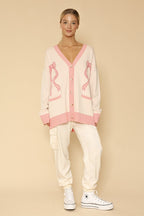 Person wearing a pink cardigan with bow designs on a beige background