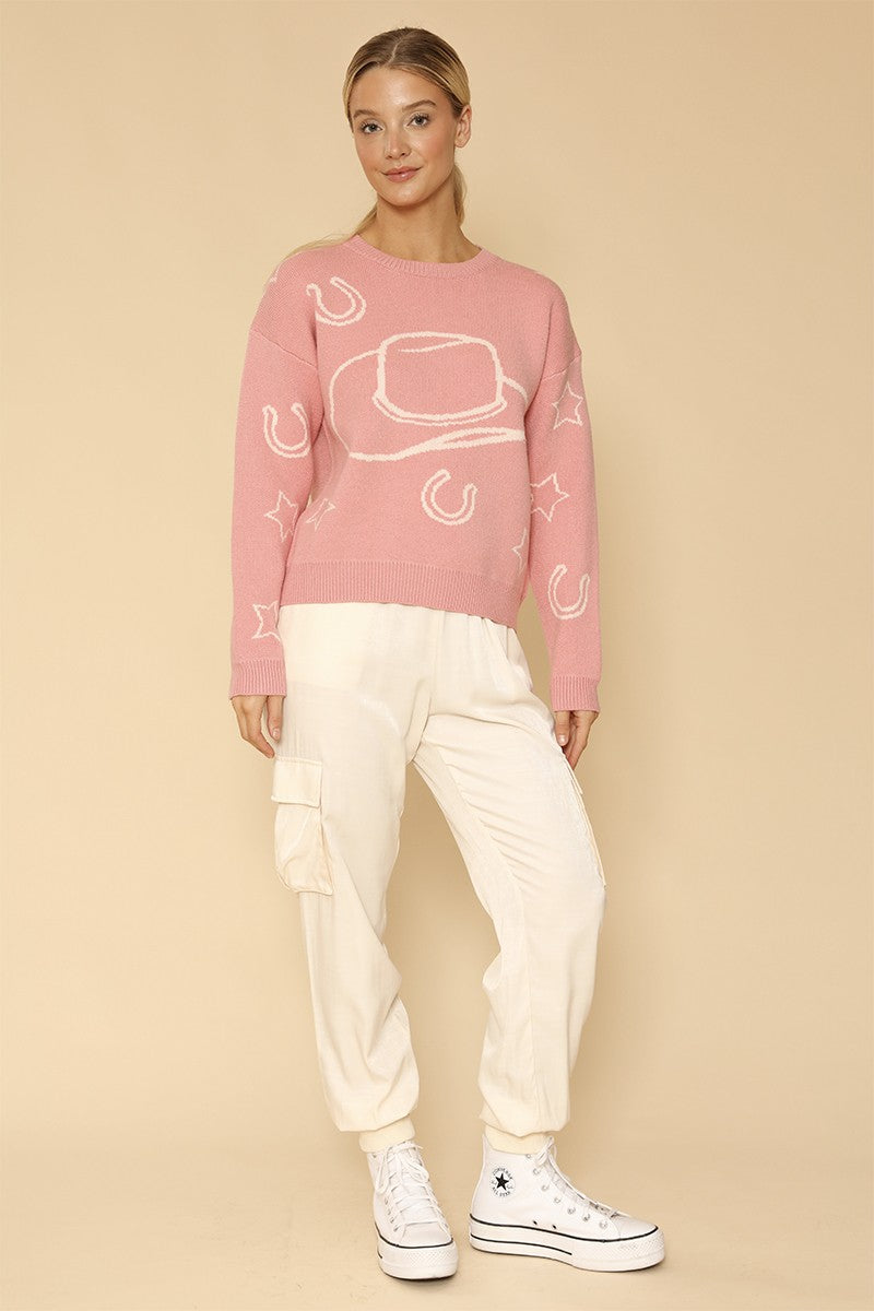 Person wearing a pink sweater with white graphics and white pants on a beige background