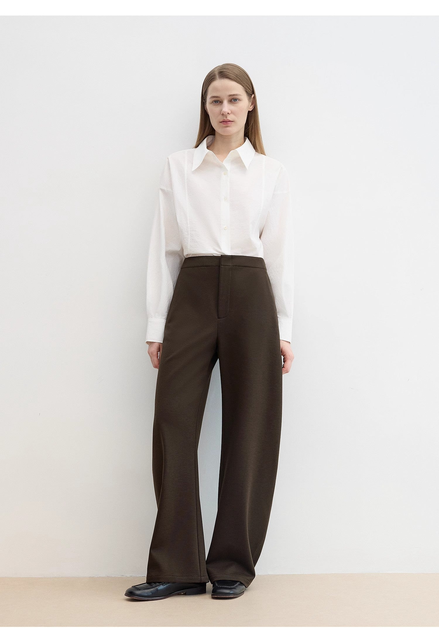 Woman wearing a white shirt and brown pants on a plain background